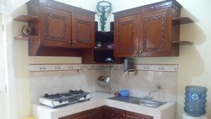 A compact kitchen with wooden cabinets, a gas stove, a sink, and a water dispenser. - Villa Kota Bunga Mawar (Cipanas)