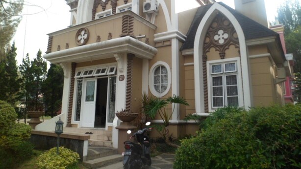 A building with a symmetrical facade, large arched windows, and a central entrance with a door. - Villa Kota Bunga Mawar (Cipanas)