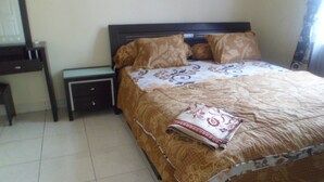 A bedroom with a bed, a nightstand, a desk, and a chair. - Villa Kota Bunga Mawar (Cipanas)