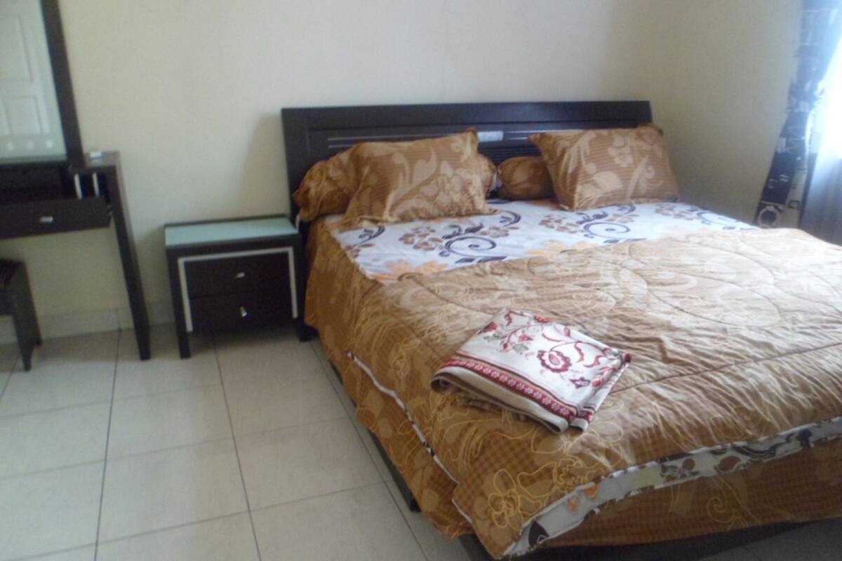 A bedroom with a bed, a nightstand, a desk, and a chair.