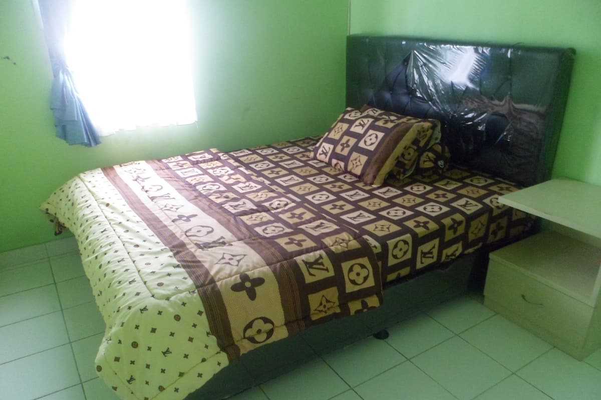 A bedroom with a bed, a nightstand, and a window with curtains.