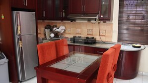 A compact kitchen with a refrigerator, stove, and dining table. - Villa Kota Bunga Peony (Cipanas)