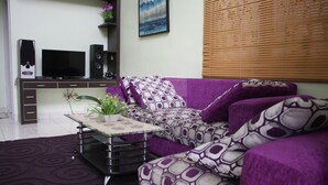 A living room with a purple sofa, a glass coffee table, a TV, and a speaker system. - Villa Kota Bunga Peony (Cipanas)