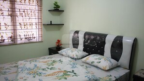 A neatly made bed with floral bedding, a black and white headboard, and a window with blinds. - Villa Kota Bunga Peony (Cipanas)