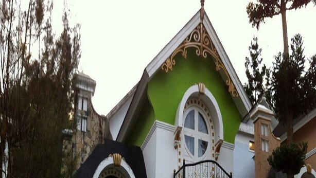 A two-story house with a green and white exterior, stone accents, and a balcony with ornate railings. - Villa Kota Bunga Peony (Cipanas)