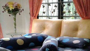 Una cama con una colcha de lunares, un florero y una ventana con cortinas.
