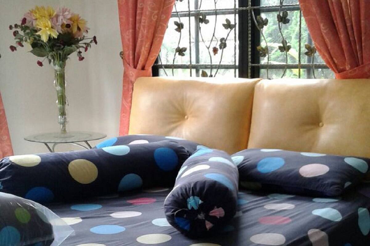 Un lit recouvert d’une couvre-lit à pois, un vase de fleurs et une fenêtre avec des rideaux.