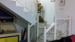Una escalera con balaustres blancos, una zona de cocina con armarios amarillos y una mesa de comedor con sillas.