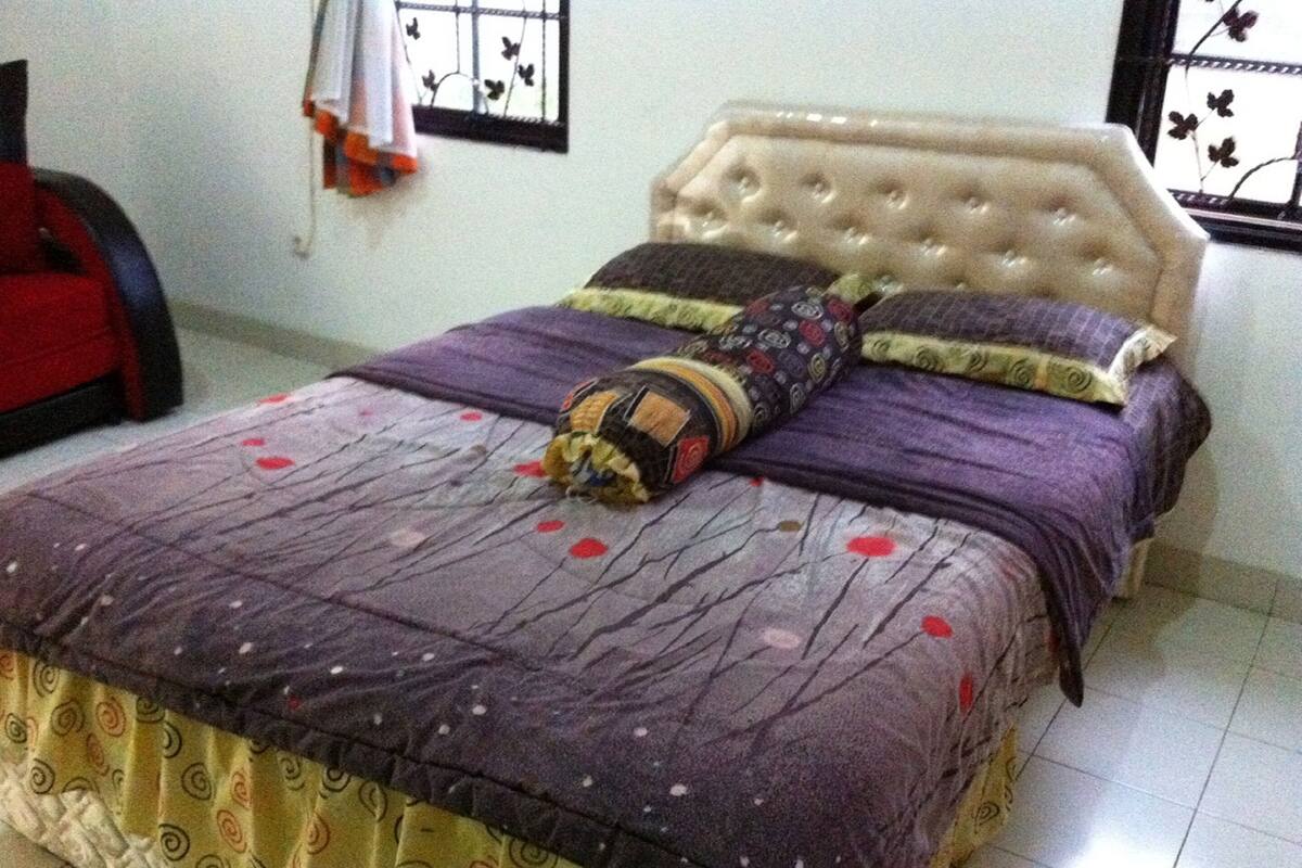 Un lit avec une couvre-lit à motifs et des oreillers, une tête de lit capitonnée et une fenêtre agrémentée d’éléments décoratifs.