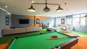 Ein Billardtisch mit Kugeln, eine Couch und ein Fernseher in einem Raum mit grünem Teppich und einer Holzvertäfelung.