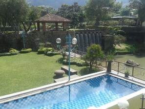 A swimming pool with a checkered pattern, surrounded by a well-maintained lawn and a small waterfall feature.