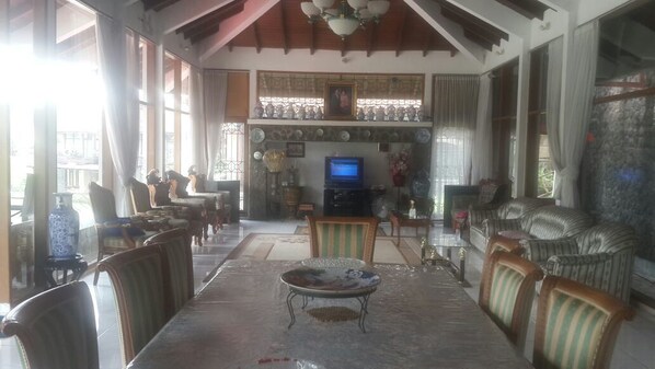 A spacious living room with a high ceiling, a television, and a variety of seating arrangements including chairs and sofas.