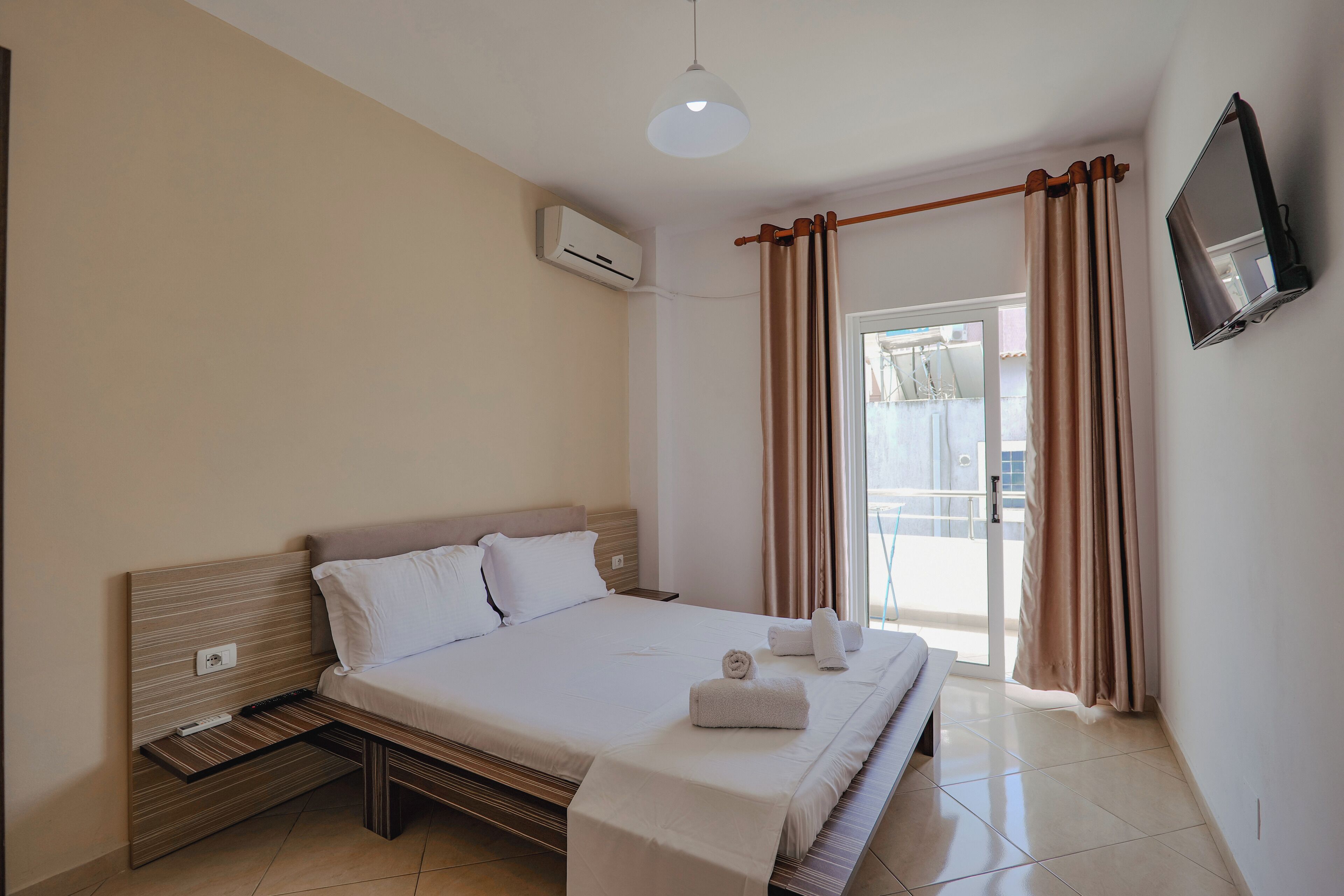 A hotel room with a bed, a TV mounted on the wall, and an air conditioning unit.