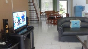 A living room with a television, speakers, a sofa, and a dining area with chairs and a table. - Villa Private Puncak (Cipanas)