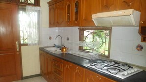 A kitchen with wooden cabinets, a gas stove, a sink, and a window with a view of greenery. - Villa Private Puncak (Cipanas)