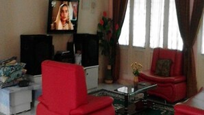 Un salon avec un fauteuil rouge, un canapé, une télévision et une table basse.