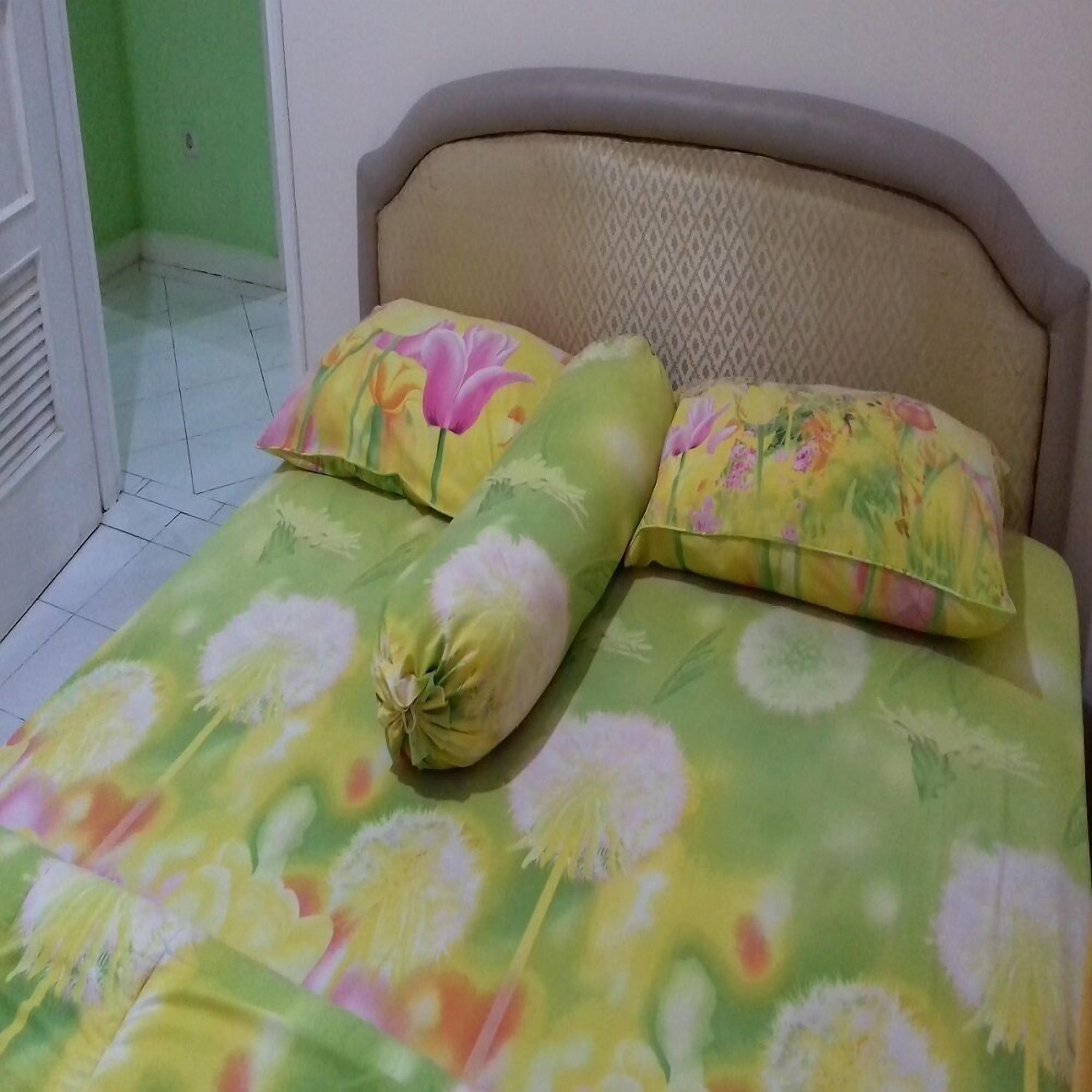 A bed with floral bedding, a headboard, and a window with a view of a green wall.