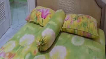 A bed with floral bedding, a headboard, and a window with a view of a green wall.