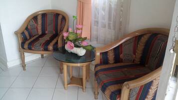 Una habitación con dos sillones de madera y una pequeña mesa redonda con un jarrón de flores.