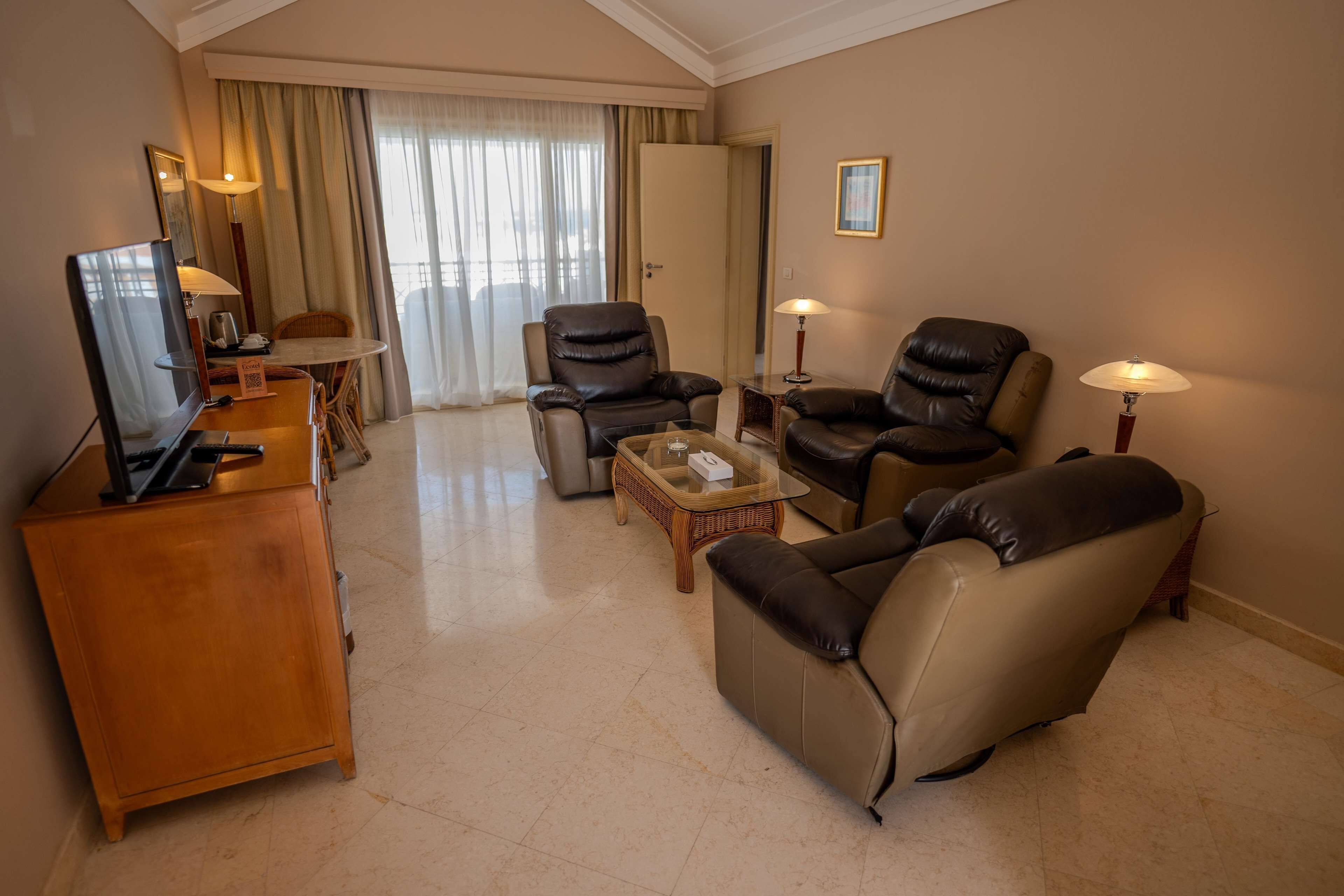 Quarto de hotel com televisão, poltronas de couro, mesa de centro e aparador de madeira.