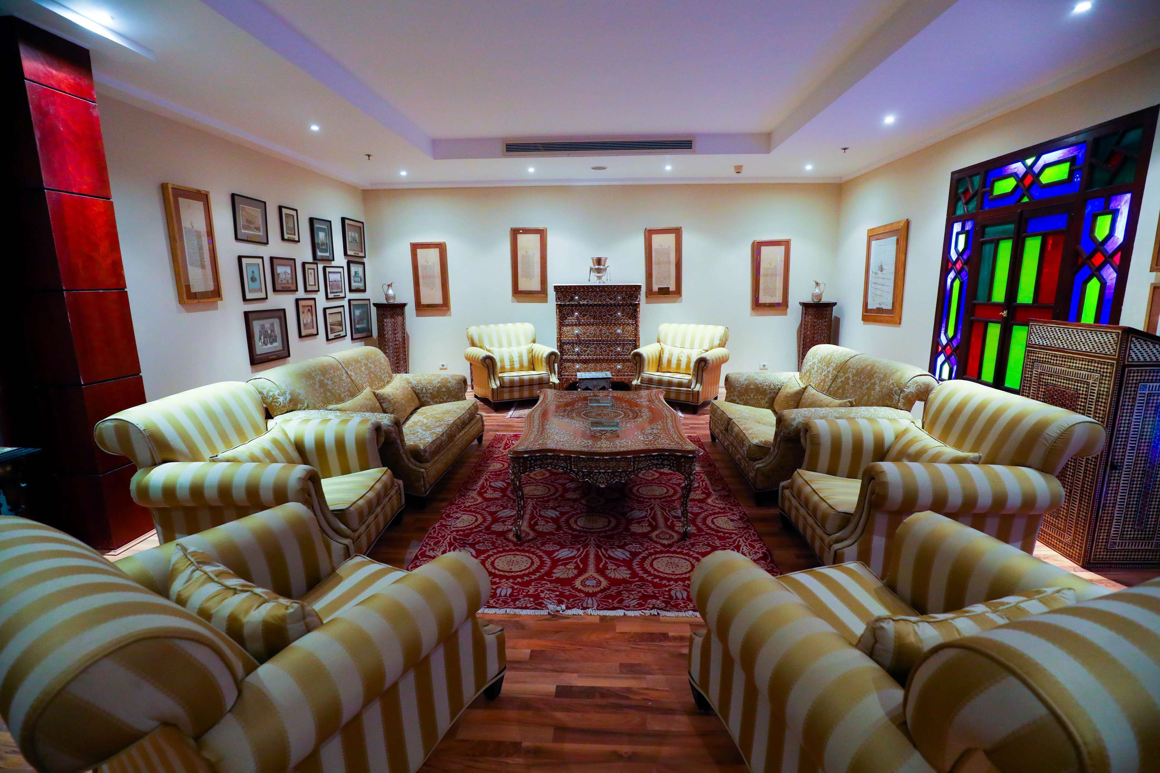 A room with striped sofas arranged around a central coffee table, framed pictures on the walls, and a stained glass window.