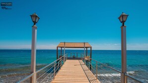 Un muelle de madera que conduce a un pabellón con dos farolas a cada lado, con vista a un mar tranquilo.