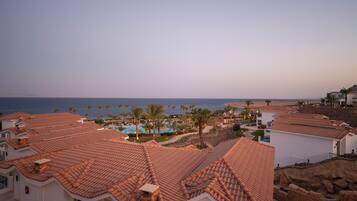 A coastal resort with terracotta-tiled buildings, a swimming pool, and palm trees.