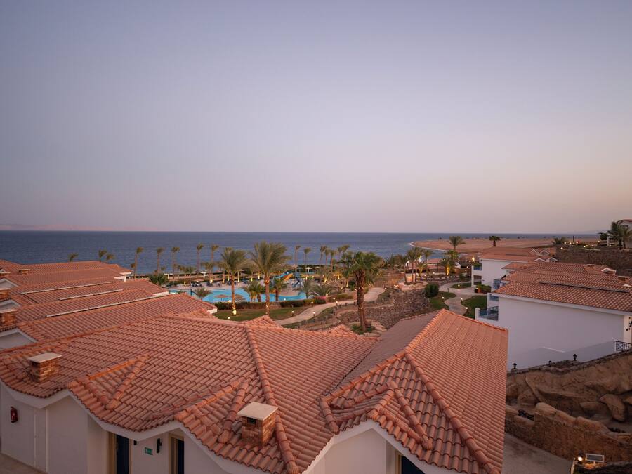 A coastal resort with terracotta-tiled buildings, a swimming pool, and palm trees.