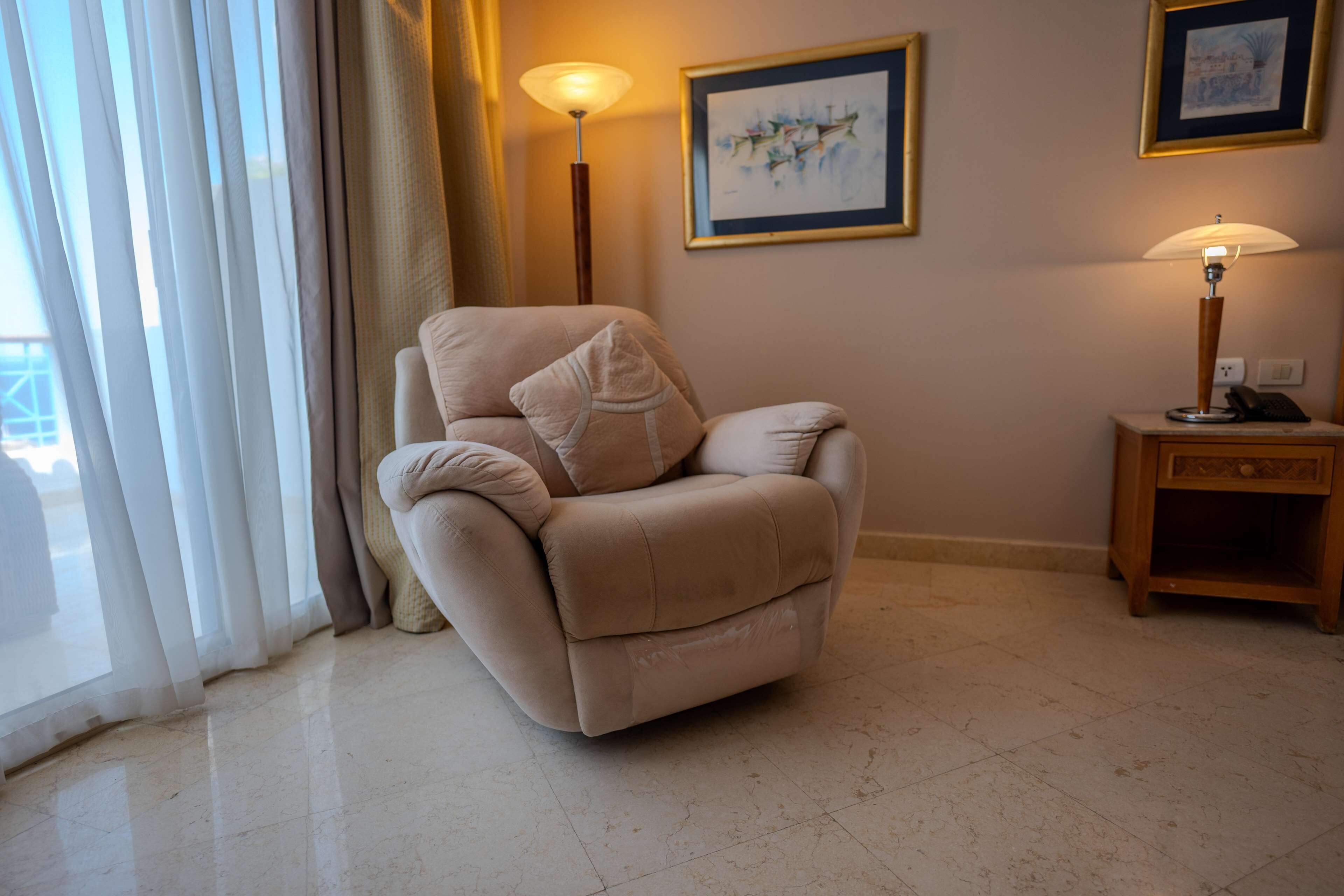 A beige armchair with a cushion, a standing floor lamp, and a framed picture on the wall.