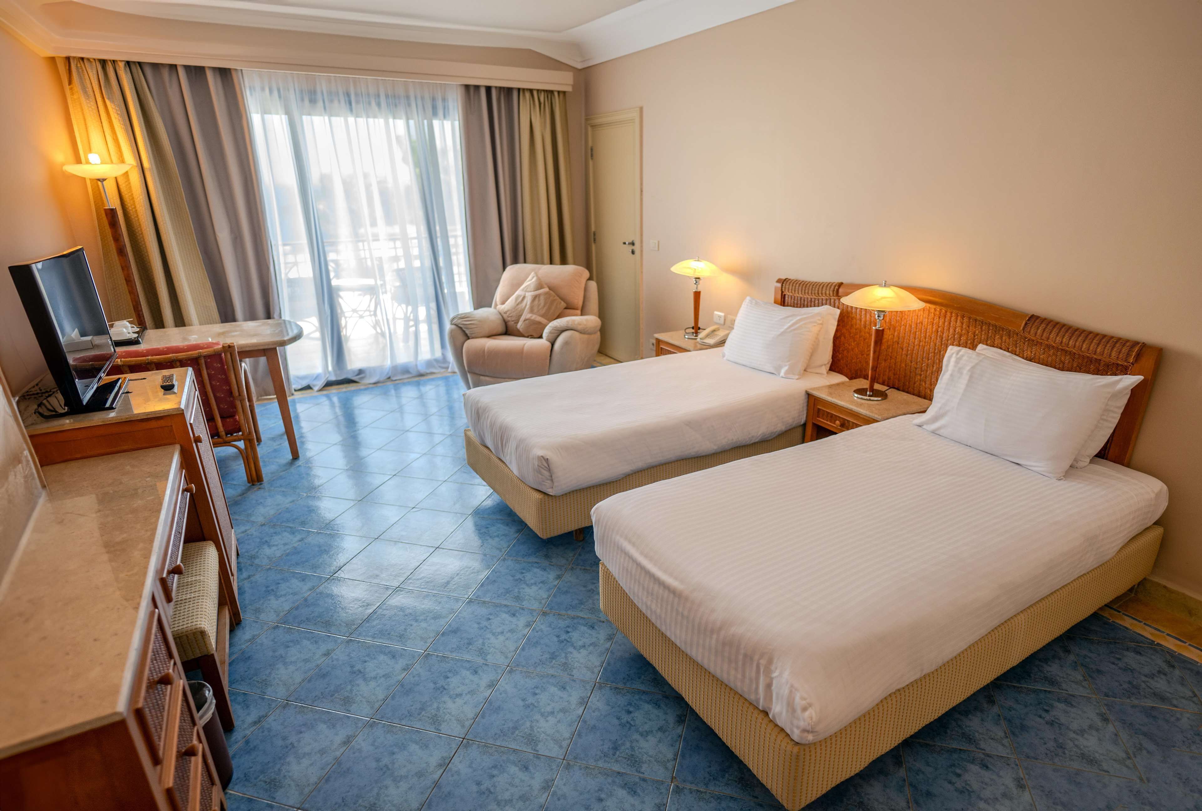 A hotel room with two beds, a desk with a computer, a chair, and a TV.
