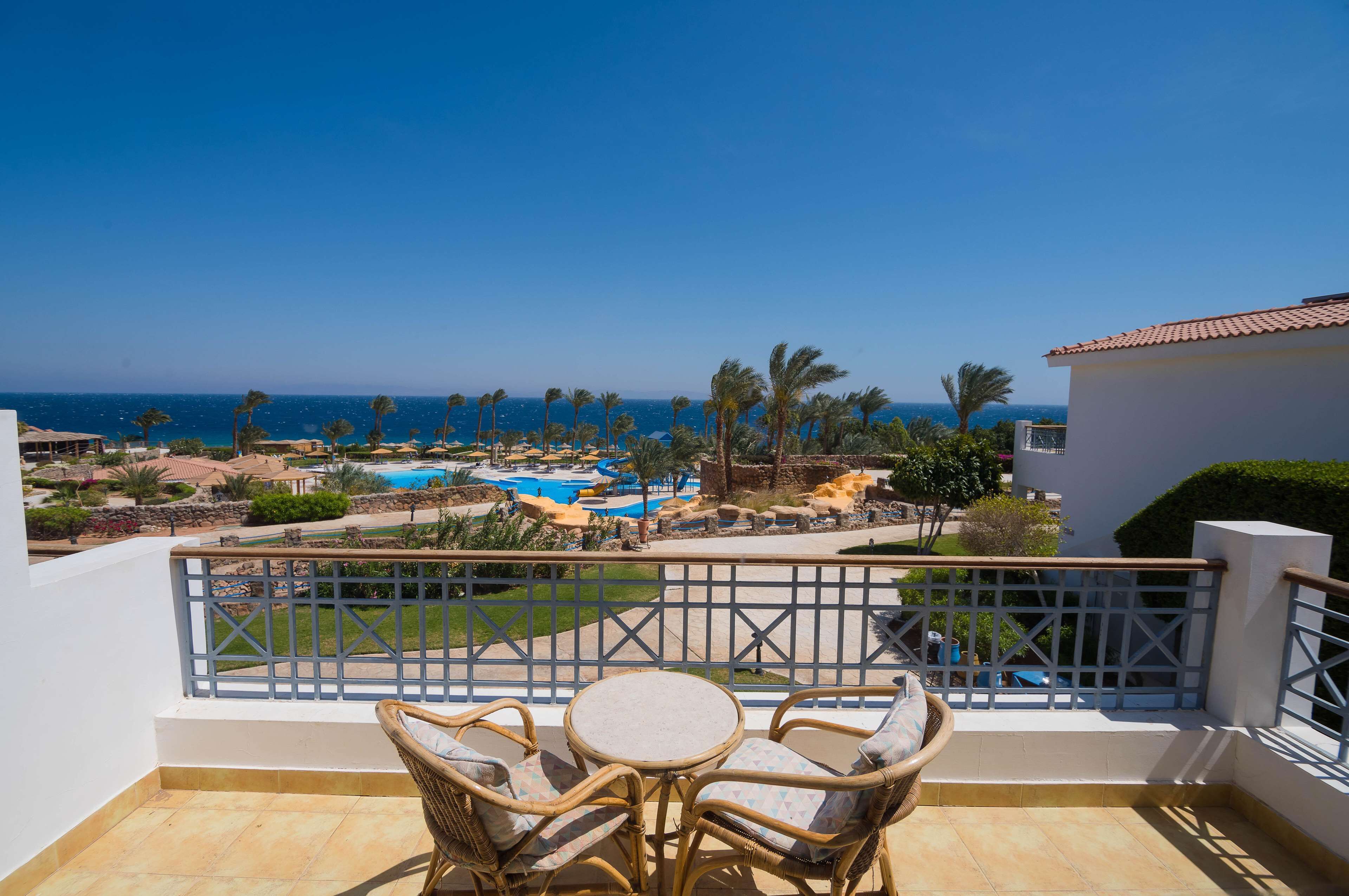 A balcony with wicker furniture, a view of a pool area, and a clear blue sky.