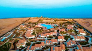 Vista aérea de un resort con varias edificaciones, una piscina central y una zona de playa.