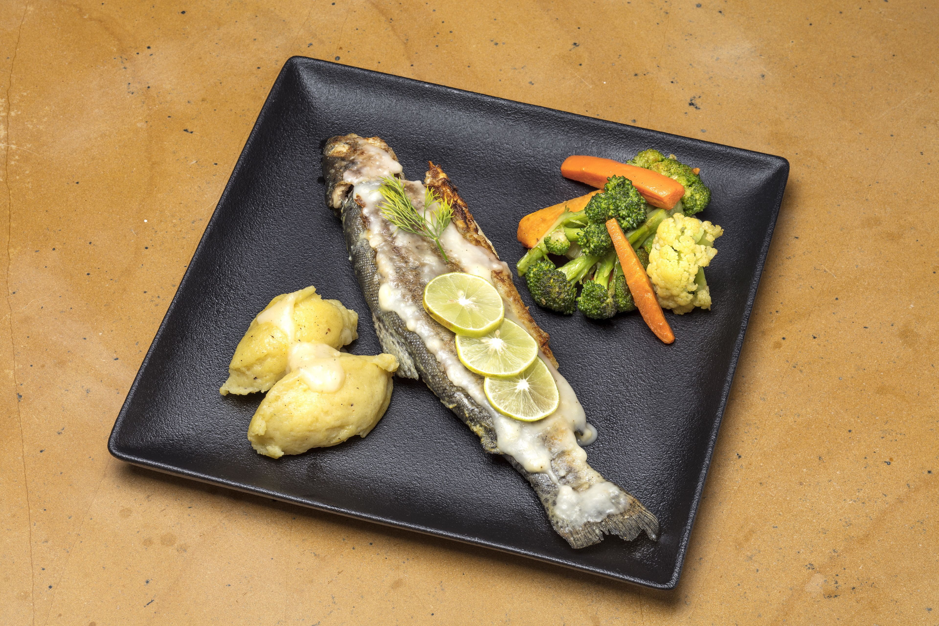 A plate with a grilled fish, lemon slices, mashed potatoes, and steamed vegetables.