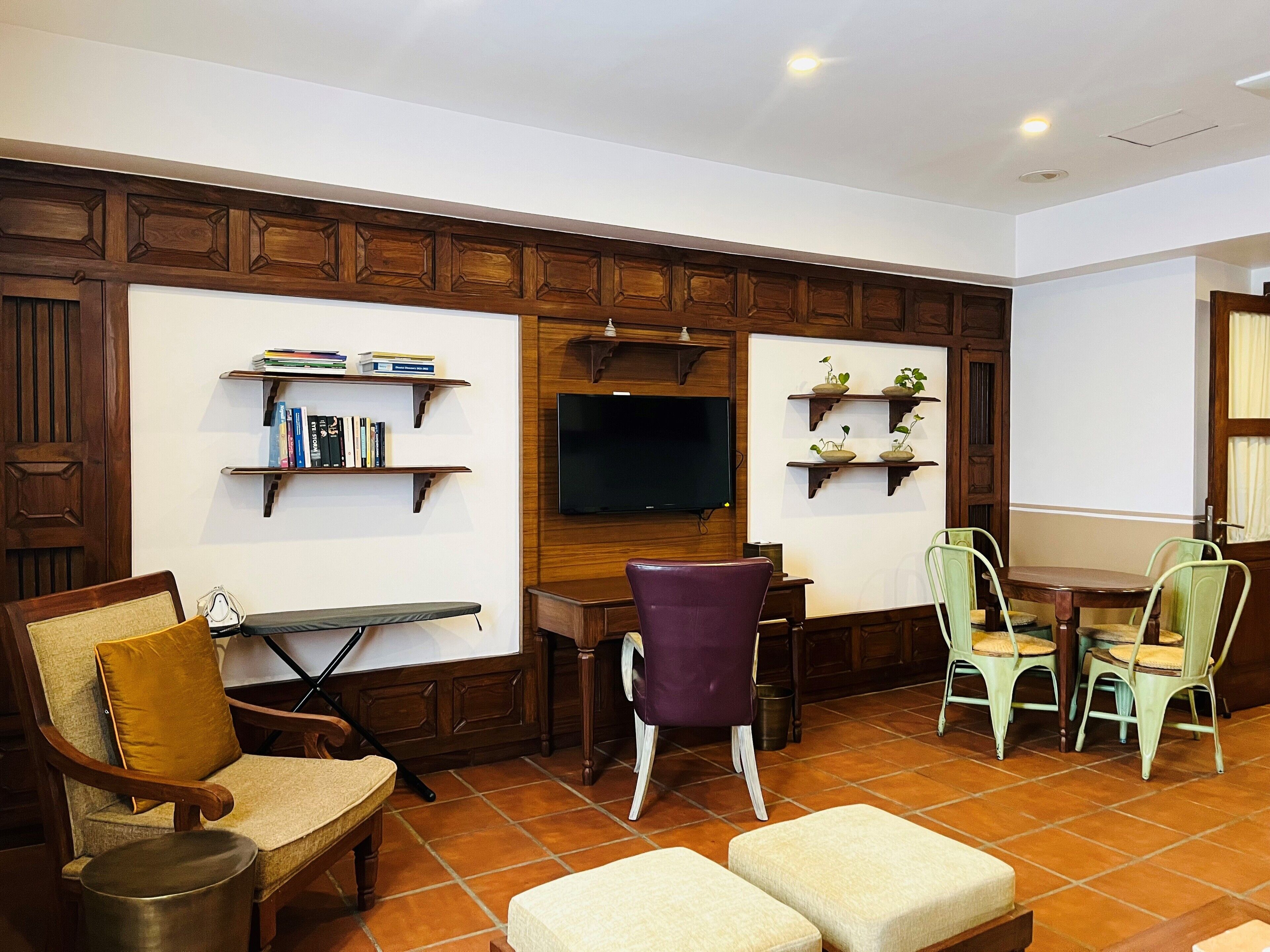 A living room with a wooden paneled wall, a flat-screen TV, a dining table with chairs, and a bookshelf.