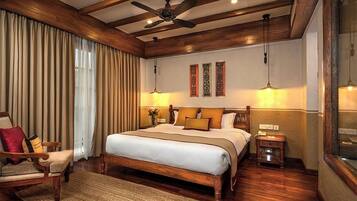 A spacious bedroom with a large bed, wooden ceiling beams, a ceiling fan, and a nightstand with a lamp.