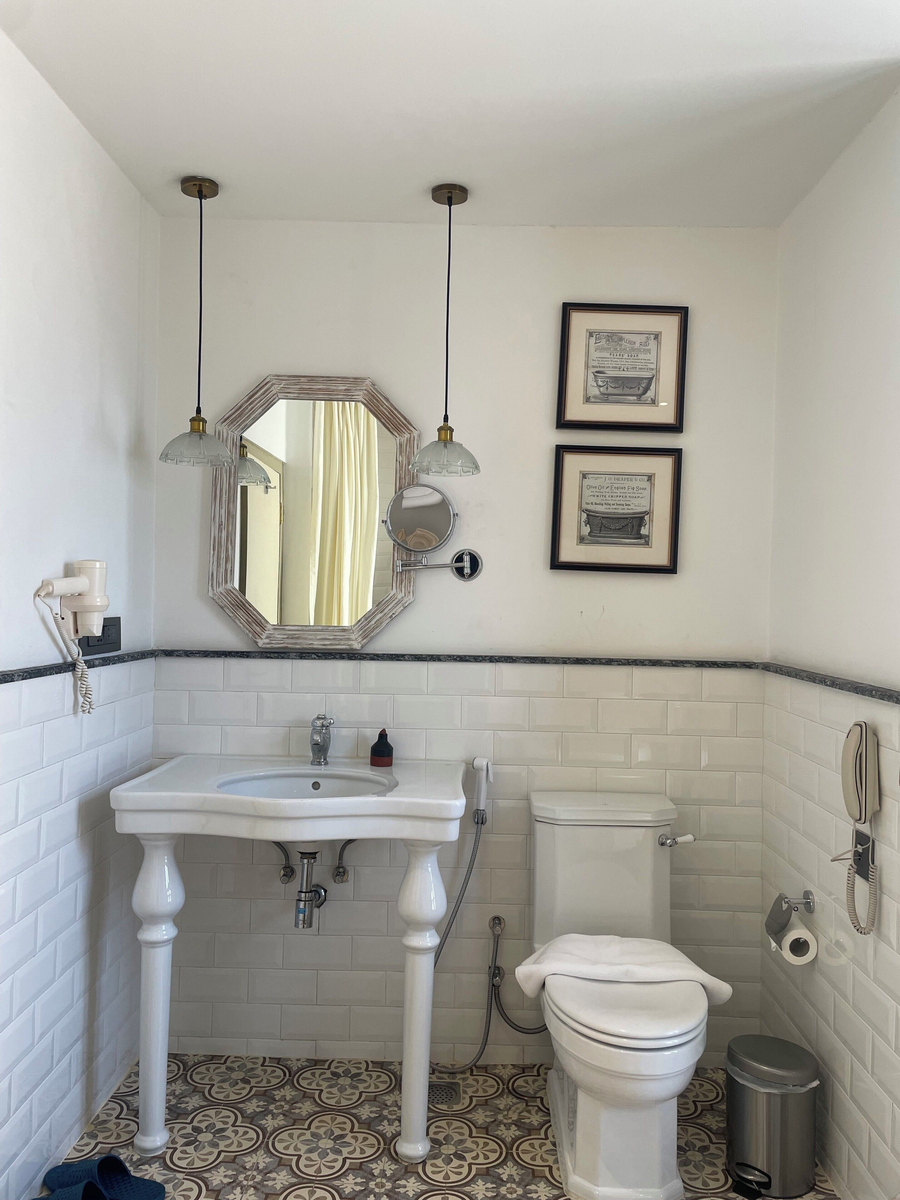 A bathroom with a white sink, a toilet, a mirror, and two framed pictures on the wall.