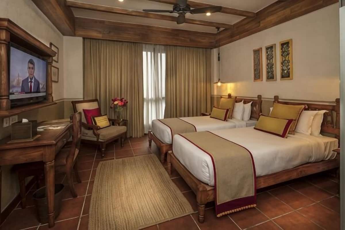 Una habitación de hotel con dos camas, un escritorio, un televisor y un ventilador de techo.