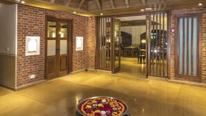 A spacious lobby with a high ceiling and wooden beams, a central flower arrangement, and a view of the dining area. - Nepali Ghar Hotel, Thamel – Your Home in Nepal (Kathmandu)