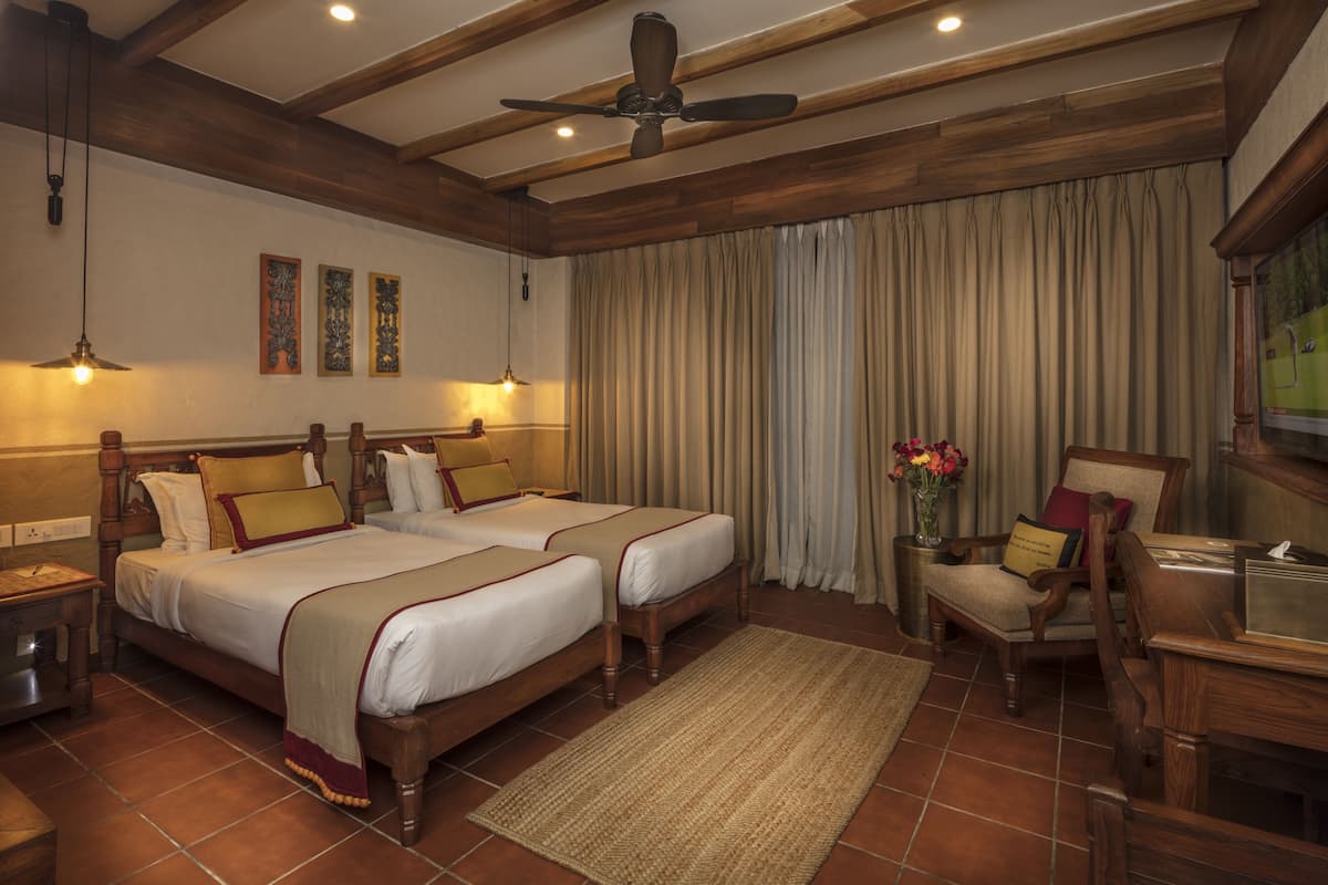 Habitación de hotel con dos camas, cabeceros de madera, ventilador de techo y un gran ventanal con cortinas.