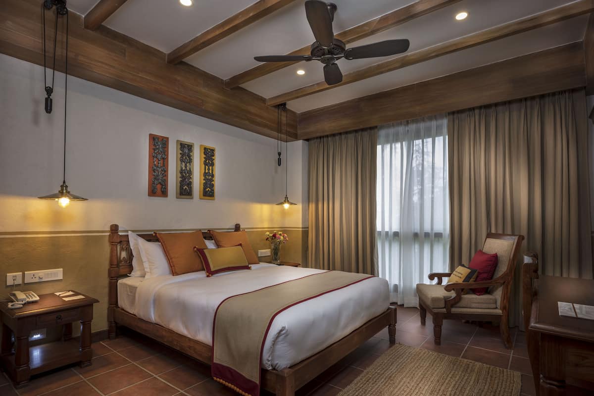 Un dormitorio amplio con una cama grande, cabecera de madera, ventilador de techo y vistas al exterior a través de cortinas translúcidas.