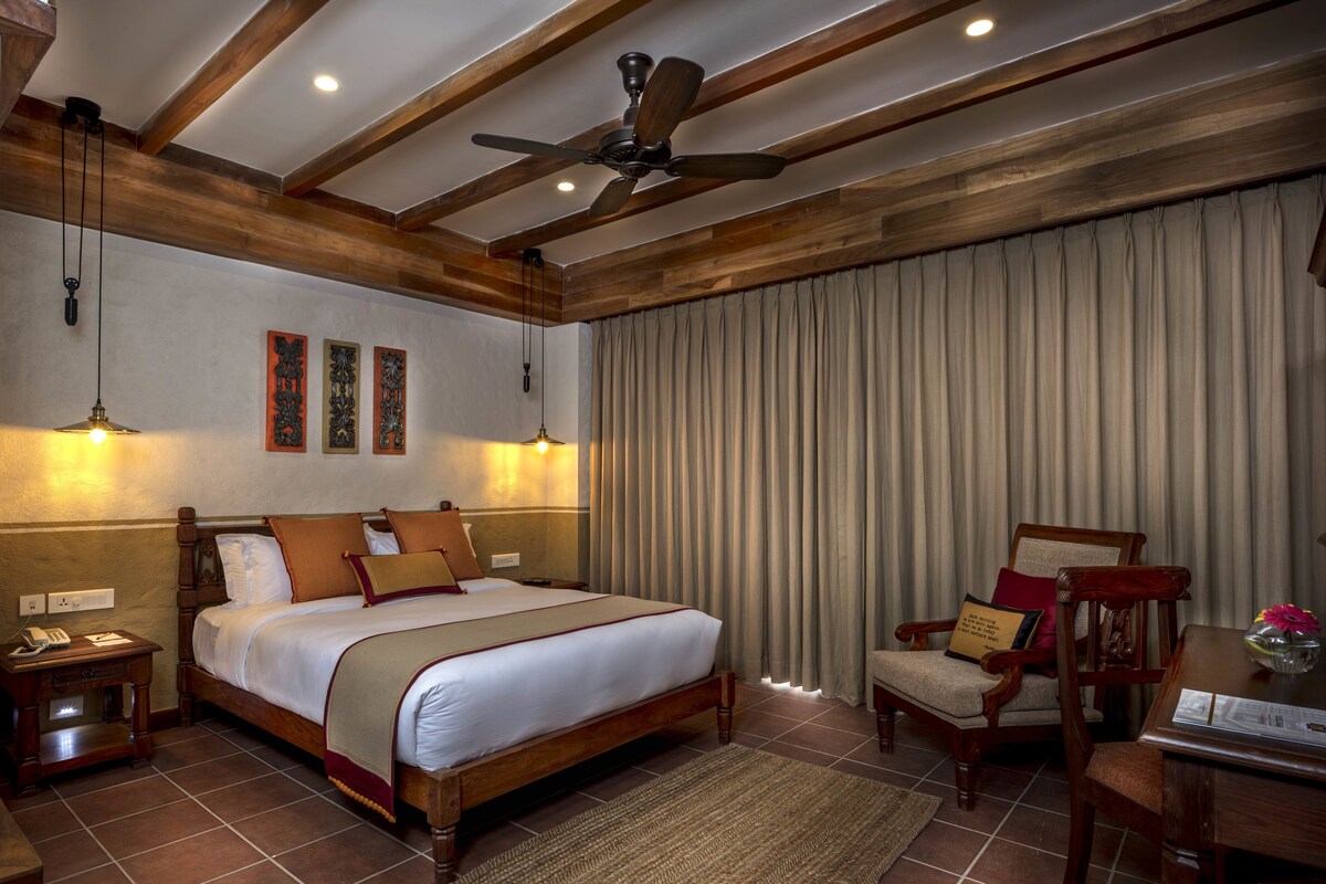A bedroom with a wooden bed, a ceiling fan, a desk with a chair, and a large window with curtains.