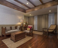 Un salón con un banco de madera, un sofá, una silla y una pequeña mesa. Hay una lámpara sobre la mesa y un jarrón con flores. La habitación tiene vigas de madera en el techo y una ventana con cortinas.