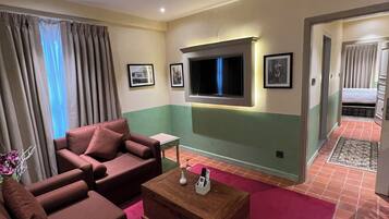 Une chambre d’hôtel équipée d’un canapé, d’un téléviseur fixé au mur et d’une petite table sur laquelle se trouvent un vase et des télécommandes.