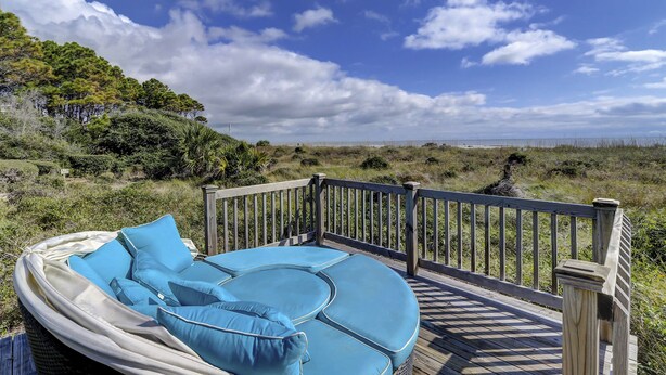 Une terrasse dotée d’un espace salon avec des coussins bleus, offrant une vue sur la plage et le paysage côtier.