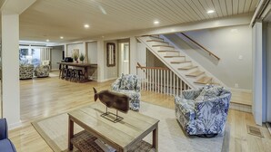 Un salon spacieux doté d’un plancher en bois, d’une table basse, de fauteuils à motifs, d’un canapé, d’un escalier et d’un coin repas avec un bar.