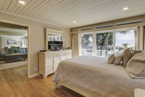 Une chambre avec un grand lit, une commode, une télévision et une vue sur les palmiers par la fenêtre.