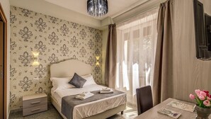 Une chambre d’hôtel avec un lit, une table de chevet, une chaise et un bureau agrémenté d’un vase de fleurs.