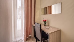 Une chambre d’hôtel avec un bureau en bois, une chaise, un miroir et un vase de fleurs.