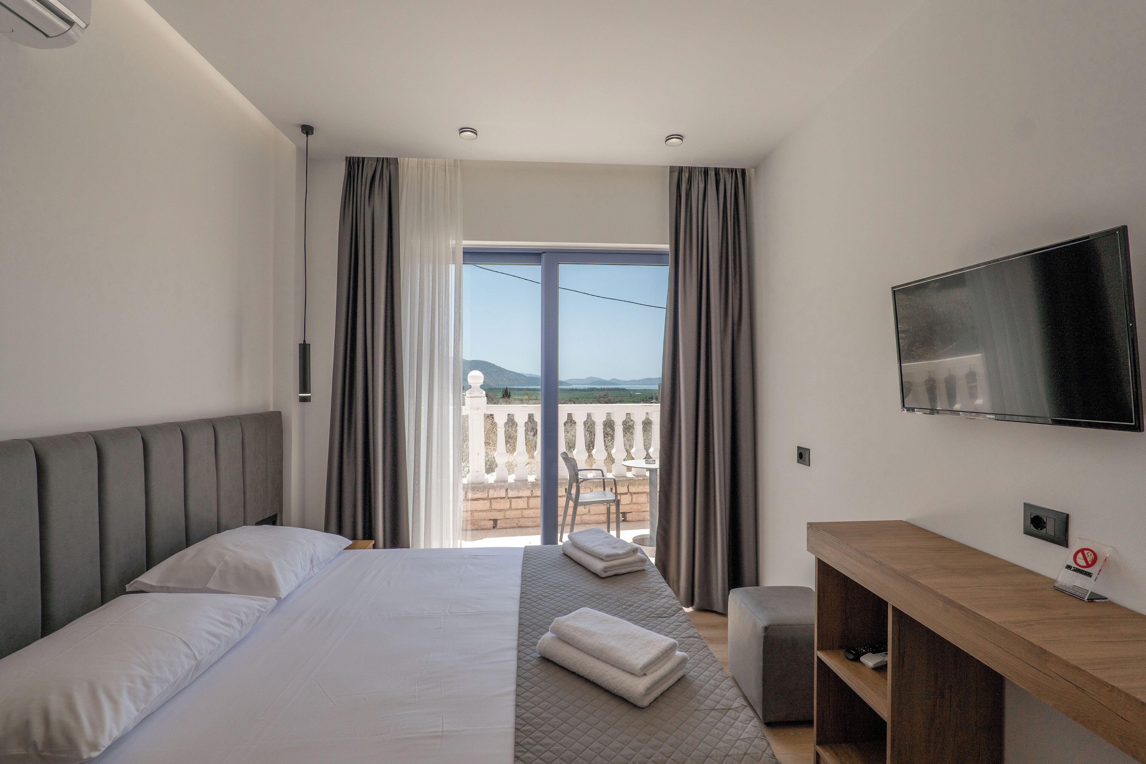 A hotel room with a bed, a desk, a TV, and a balcony with a view.
