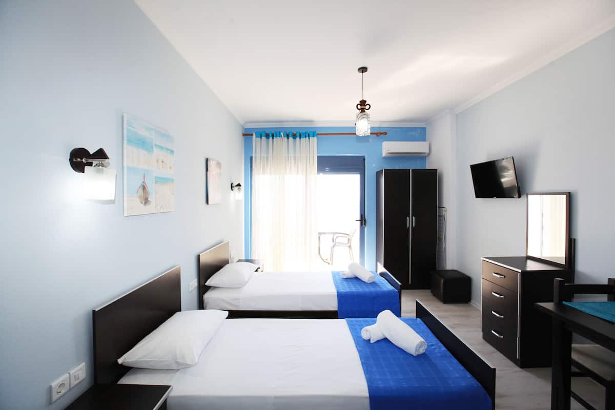A hotel room with two beds, a desk, a chair, a TV, and a wardrobe.